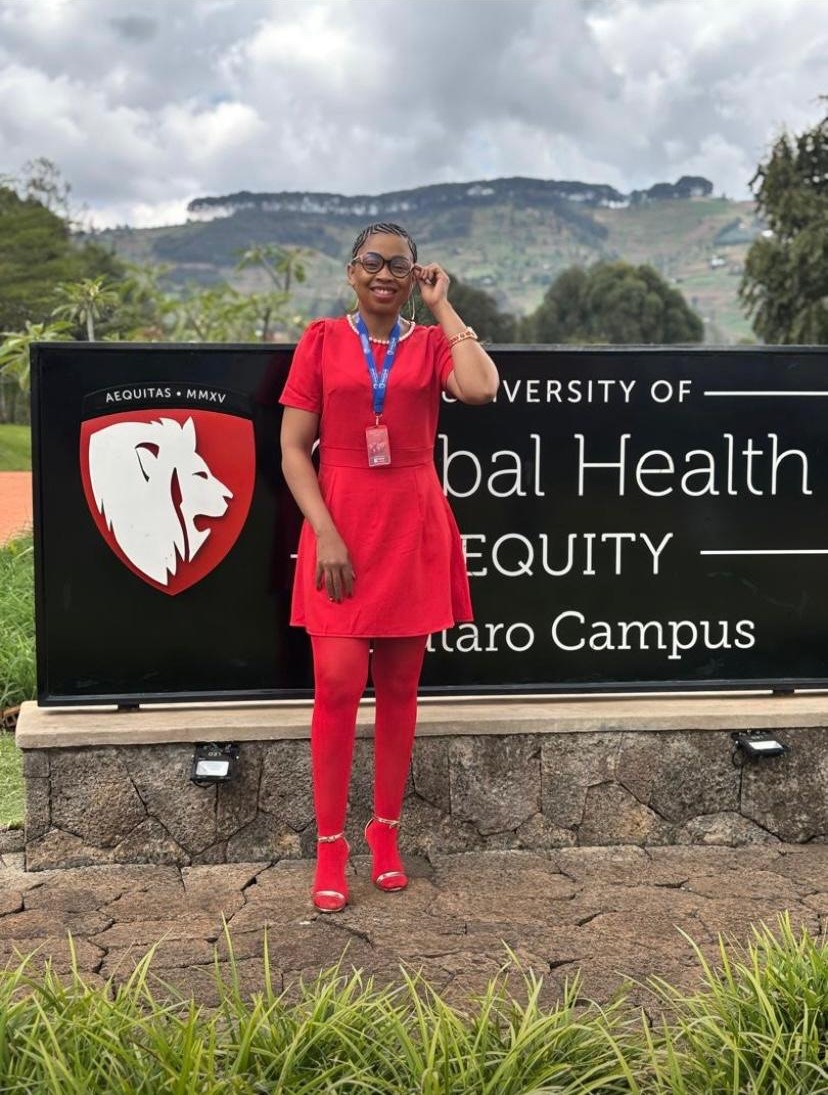 Mathato Aumane in a red dress at the University of Global Health Equity campus sign