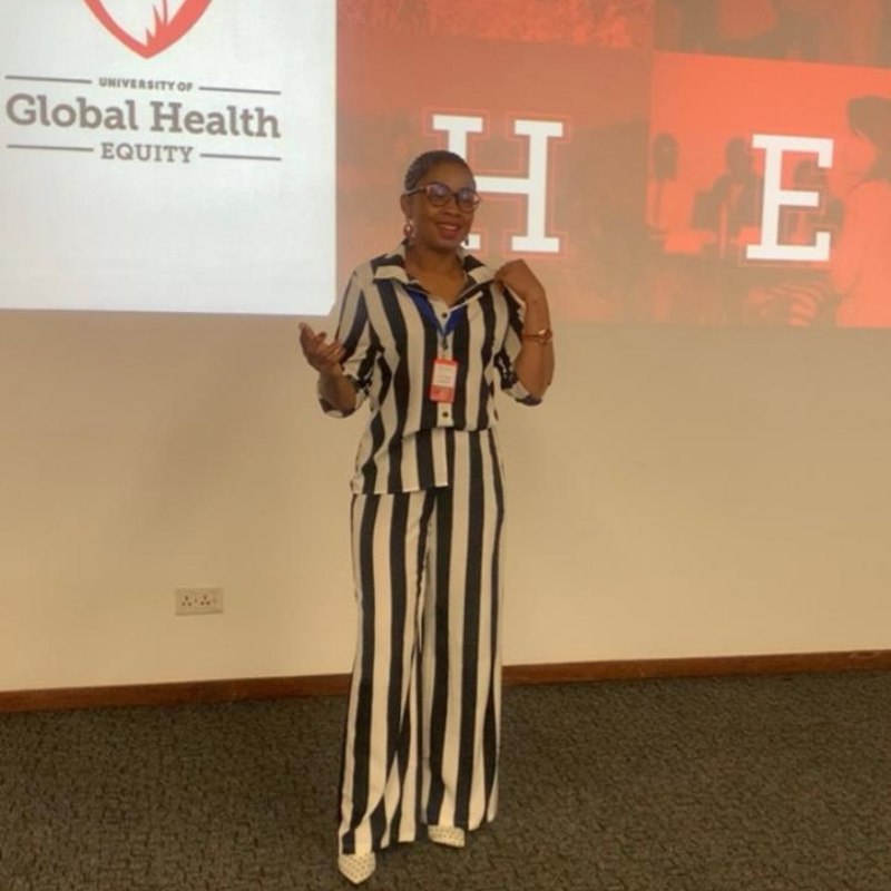 Mathato Aumane presenting on stage in a striped suit at the University of Global Health Equity